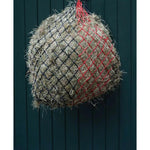 Hay bale wrapped in netting with red and black lines against a dark wooden background