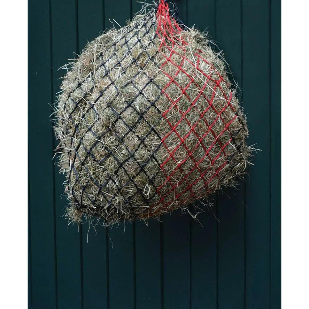 Hay bale wrapped in netting with red and black lines against a dark wooden background