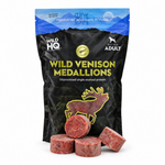A bag of Wild HQ Wild Venison Medallions pet food, with four raw, round reddish-brown meat medallions displayed in front of the black and blue packaging on a white background.